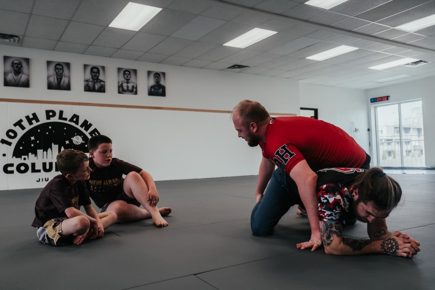 Coach Zack Holycross demonstrating a no-gi position while kids students watch from the mat at 10th Planet Columbus.