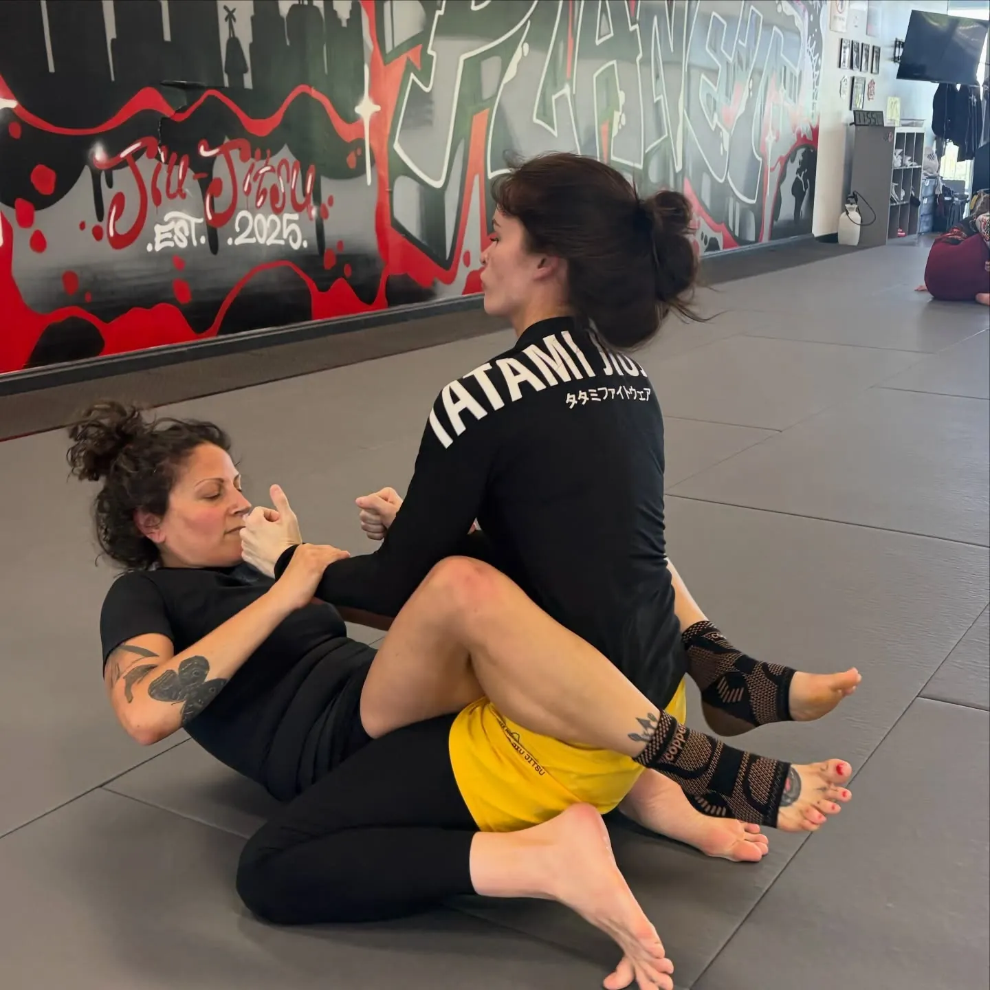 Two women training no-gi Jiu-Jitsu on the mats at 10th Planet Columbus, one working from guard while the other passes