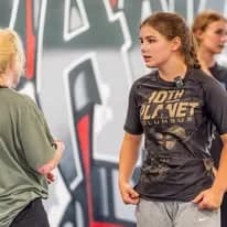 Young woman in a 10th Planet Columbus shirt listening to instruction during training